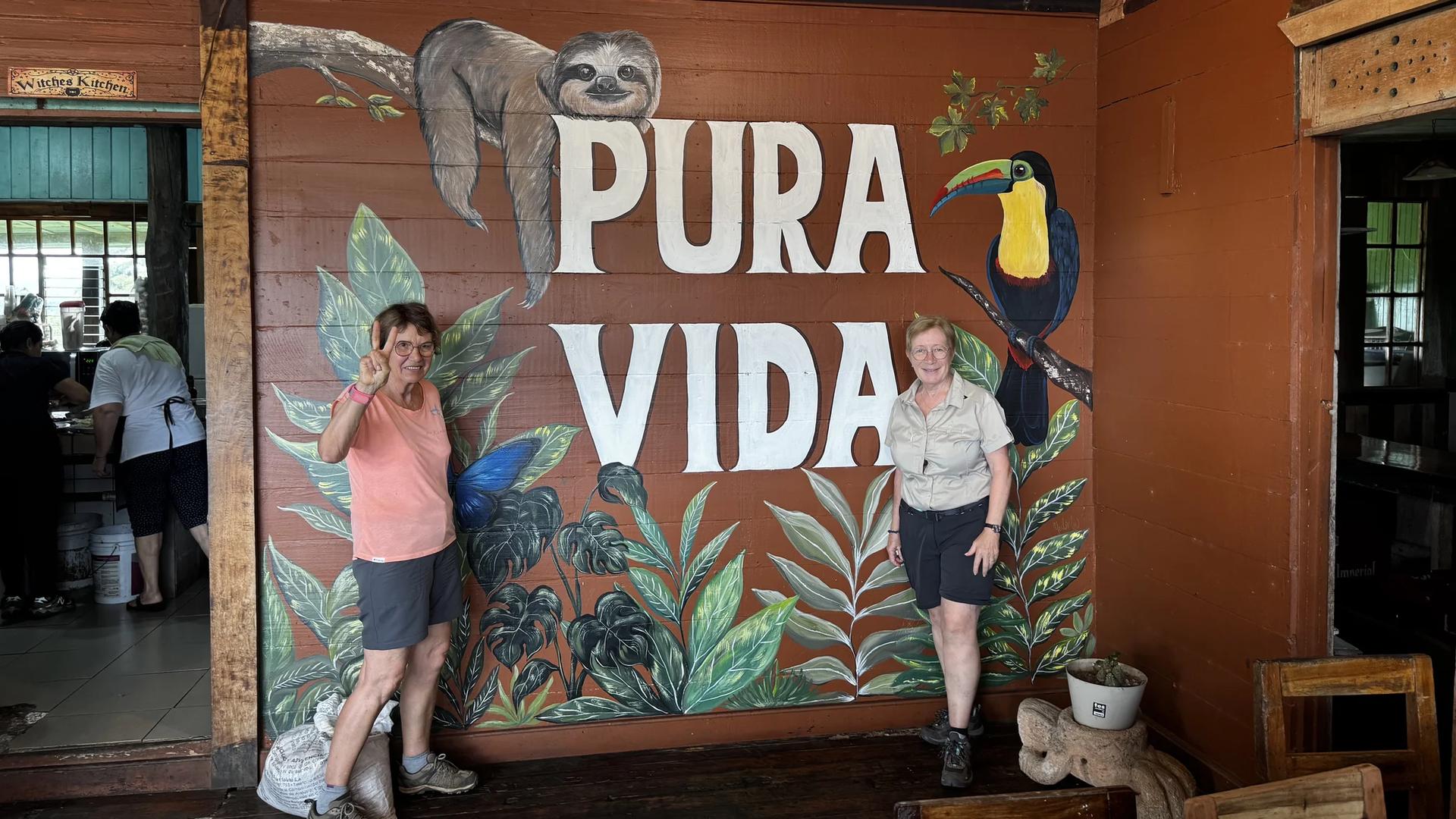 deux voyageuses devant le terme pura vida dessiné dans une ambiance locale au costa rica
