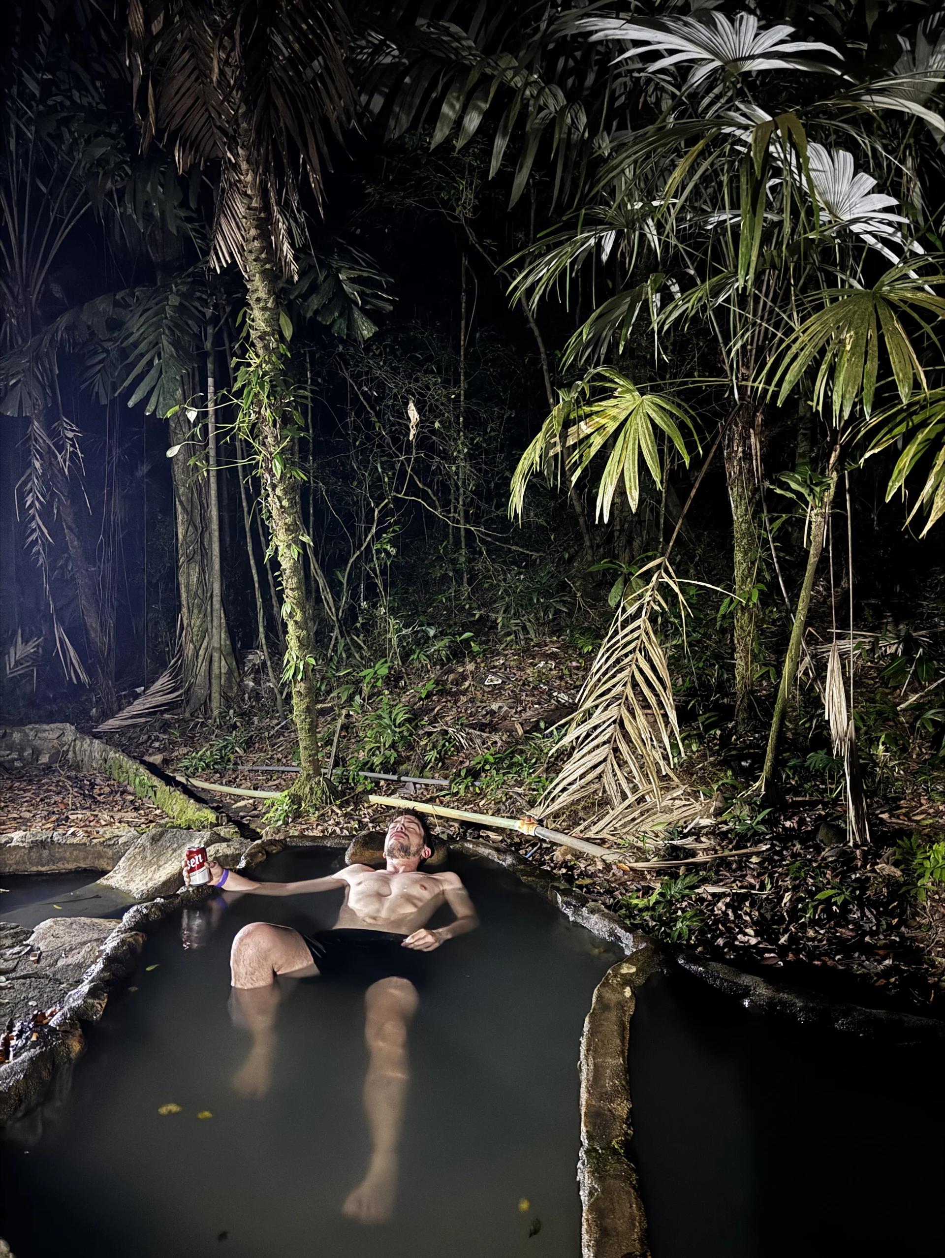 Un voyageur se relaxant dans les eaux thermales la nuit au milieu de la jungle